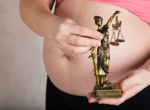 pregnant woman holding a figurine of a justice woman